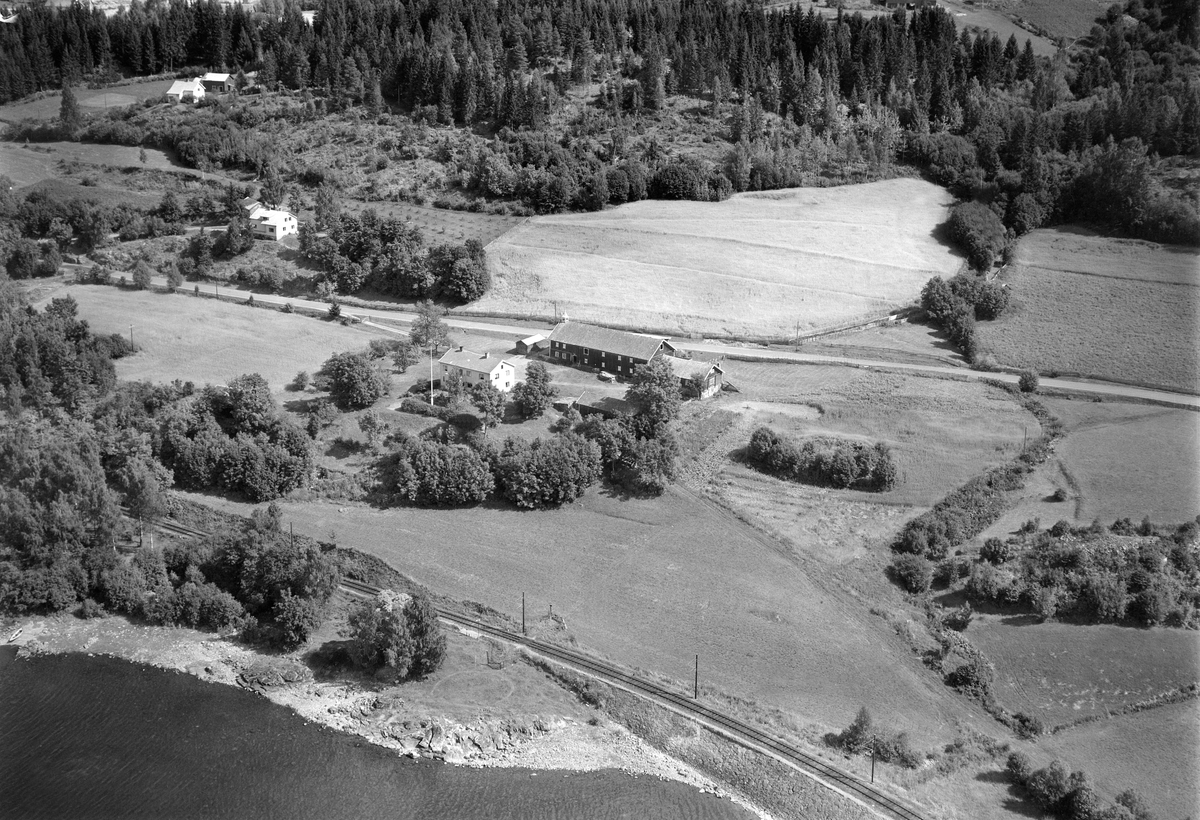 Widerøes Flyveselskap A/S, NEDRE MOSTUE (MORSTU) GÅRD, STRANDLYKKJA, Flyfoto av den gamle gjestgiver og skysstasjonsgården. Låven ble revet i 1957 for å gi plass til utvidelse av riksveg 50 som ble anlagt forbi her ca. 1963-65. Fra nederste høyre hjørnet og på skrå oppover til gårdstunet gikk den gamle Kongevegen. Gården er …
