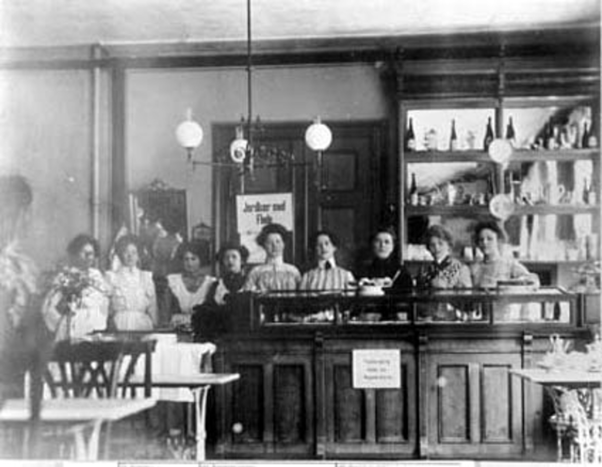 Anno Domkirkeodden, INTERIØR: GRÆNDSECAFEEN, CHRISTIANIA, GRUPPE: 9 DAMER VED DISKEN, NR 2 FRA VENSTRE: MARIE KNUDSEN RASEN, KOLDJOMFRU, (ESPA)