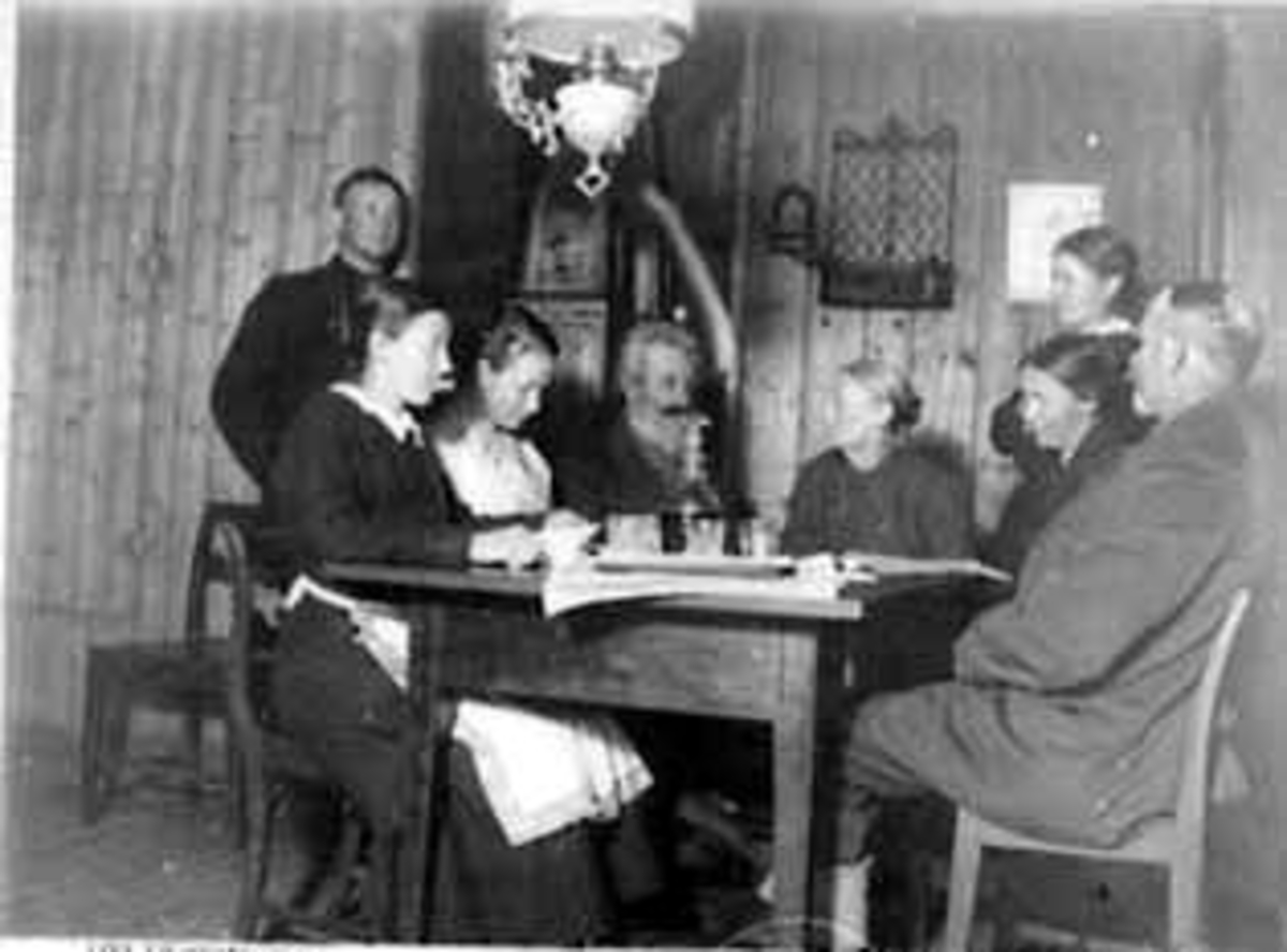 Anno Domkirkeodden, Interiør: stue, Torpet, Nord Odal, gruppe: 8, familiene Torpet og Bjølseth, fra venstre: Alf Bjølseth, Marthe Torpet, Gina Torpet, Kari Bjølseth, ole Torpet, Terese Torpet, Berthe Bjølseth, Bernhard Bjølseth, julen 1919, Bord, glass, karaffel. "Først bønn og sang, så traktering med vin og kaker. Ju…