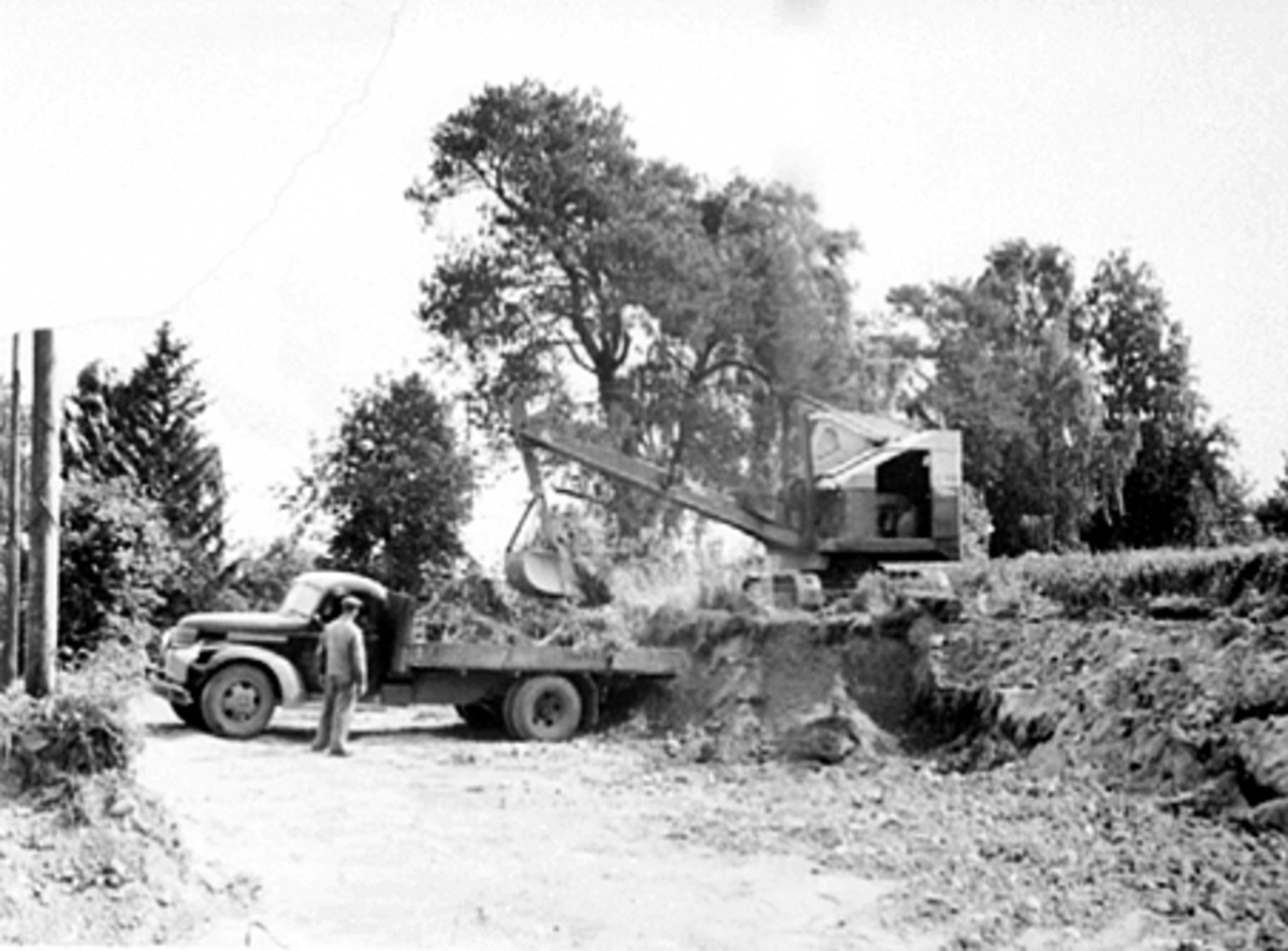 Anno Domkirkeodden, ATLUNGSTAD BRÆNDERI, UTVIDELSE AV GARDSPLASSEN, HELGE GJESTVANG KJØRER GRAVEMASKIN OG LESSER PÅ BRENNERIETS CHEVROLET LASTEBIL 1946-47 MODELL SOM KJØRES AV OLAV STRANDSBERG, BRENNERI
