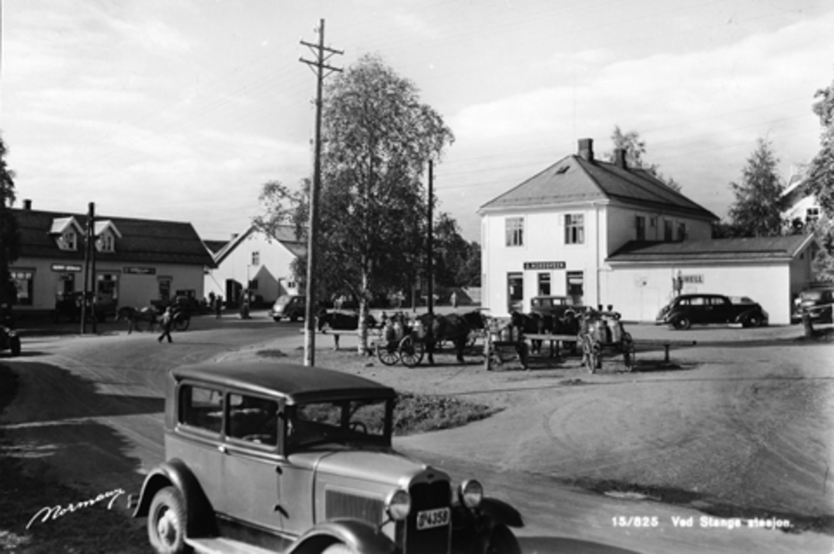 Anno Domkirkeodden, PARTI VED STANGE STASJON, BILER, HEST OG KJERRE MED MJØLKESPANN. JERNBANEGATA, MEIERITORGET, BUTIKKER, MAGNUS GODAGER, O. NORDSVEEN, BIL D-4358. Foran i bildet en Ford A 1930. Registreringsnummer D-4358. Høyeste nummer i denne Hamarserien i Norges Bilbok 1935, var 4176. To av bilene i bakgrunnen ca…