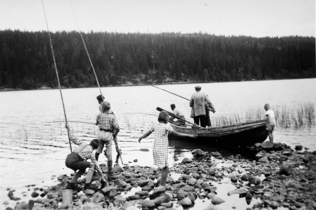 Ukjent, Matauk ved Bergsjøen i Stange 1941. 2. verdenskrig. Barn og voksne med fiskestenger, bambusstenger, markstenger, robåt.