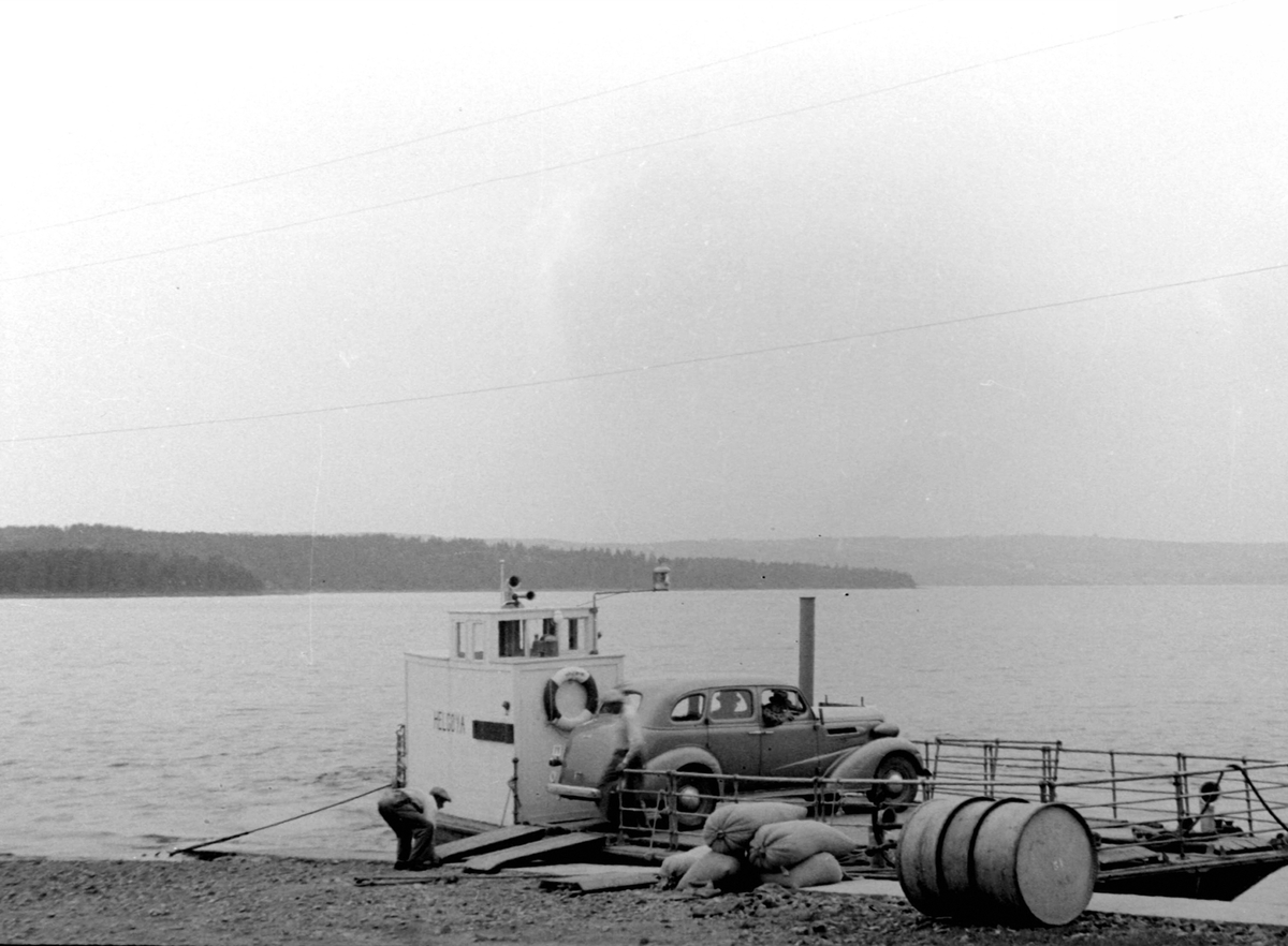 Adolf Skjegstad, Ferja M.F. Helgøya laster bil ved Nes brygge, Skurven, Helgøya i bakgrunnen.