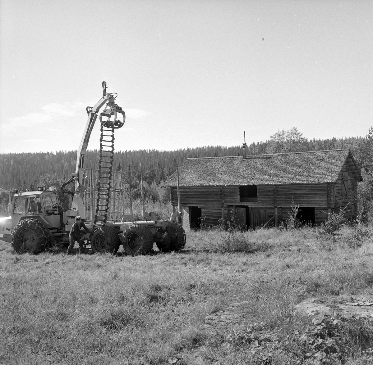 Adolf Skjegstad, En lastbærer for tømmertransport i skog. To personer legger belter på bakhjulene. Tømmerlåve.