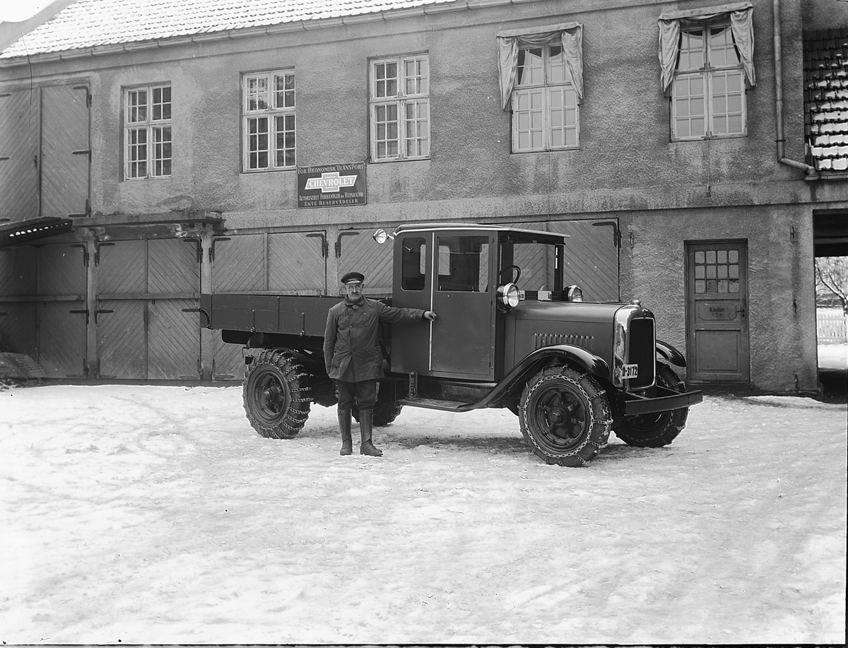 Christian Grundseth, OUSTAD MEK. VERKSTED, Hamar. LASTEBIL I BAKGÅRD, KJETTINGER. Skilt "Chevrolet" på verkstedsveggen. Registreringsnummer på lastebilen D-3172. D-3172 er en GMC eid av Hedmark fylkes veivesen.