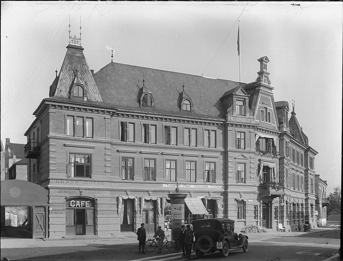 Christian Grundseth, GRAND HOTELL. HAMAR. BYGD I 1893, BLE SKADD I 1969 AV BRANN OG VEK DA PLASSEN FOR GRAND-SENTERET. EKSTERIØR. MED BIL OG FOLK I FORGRUNN. Jernbanecafeen. Drosje reistreringsnr. D-160.