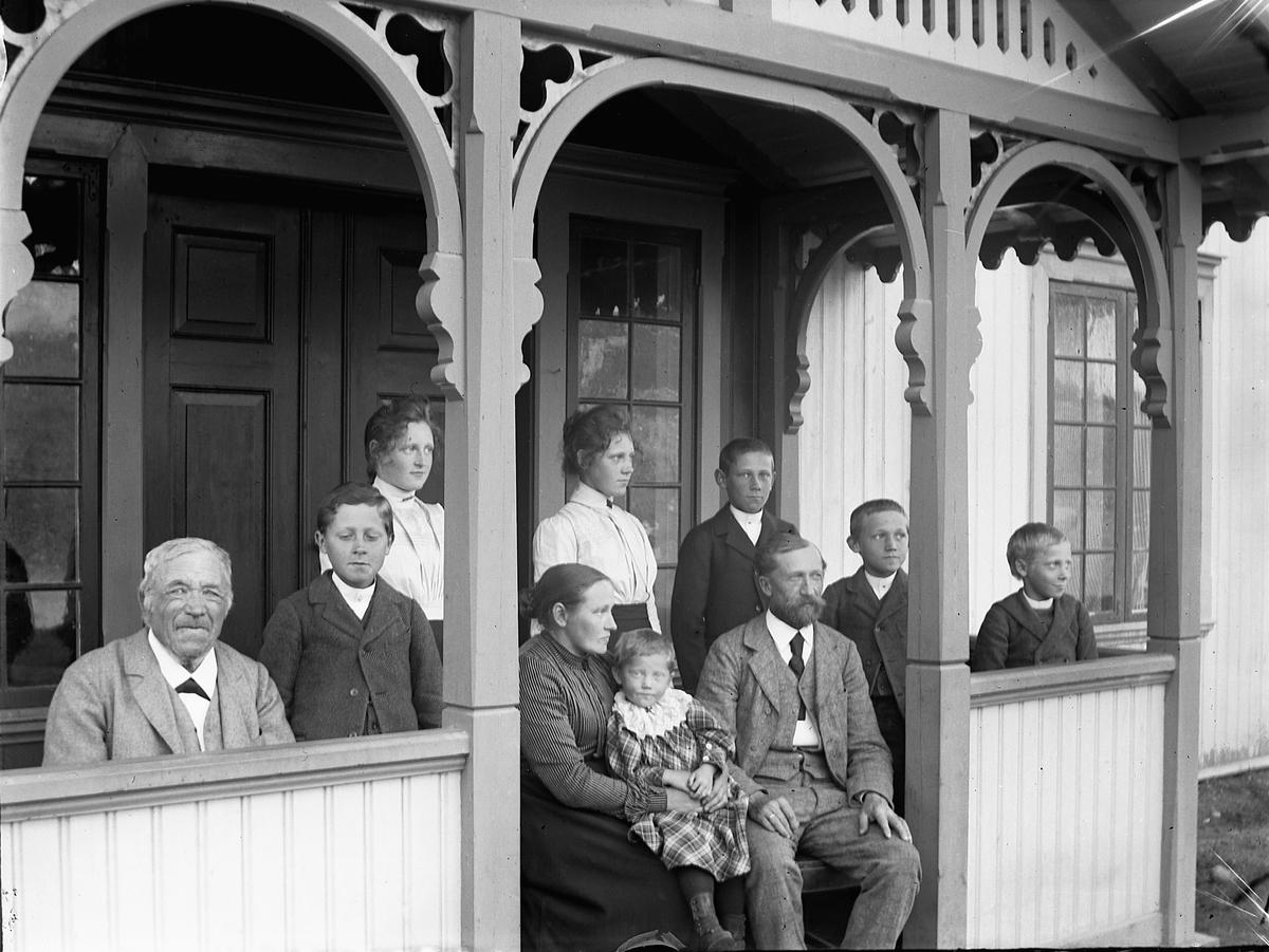Ole Hansen Løken, Familiegruppe på verandaen på Ulven, Ring. Foran fra venstre er Petter Ulven, Even, Marie, Kristiane, Mons, Hans, Aksel Mengshoel. Foran er Ingeborg Monsdatter Ulven med Petra på fanget og Bernhard Julius Mengshoel (1851-1932).