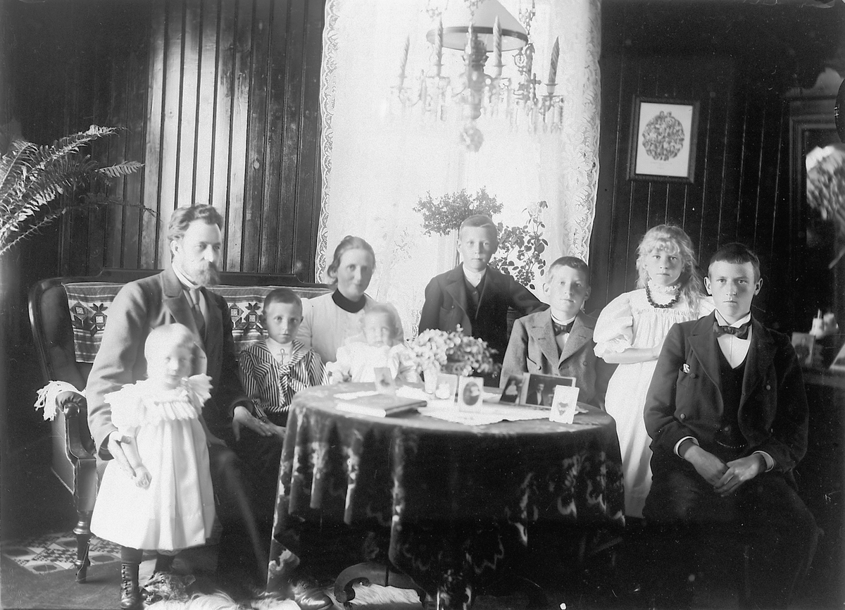 Mina Skraastad, Interiør, stue. En gruppe, familie samlet rundt stuebordet.