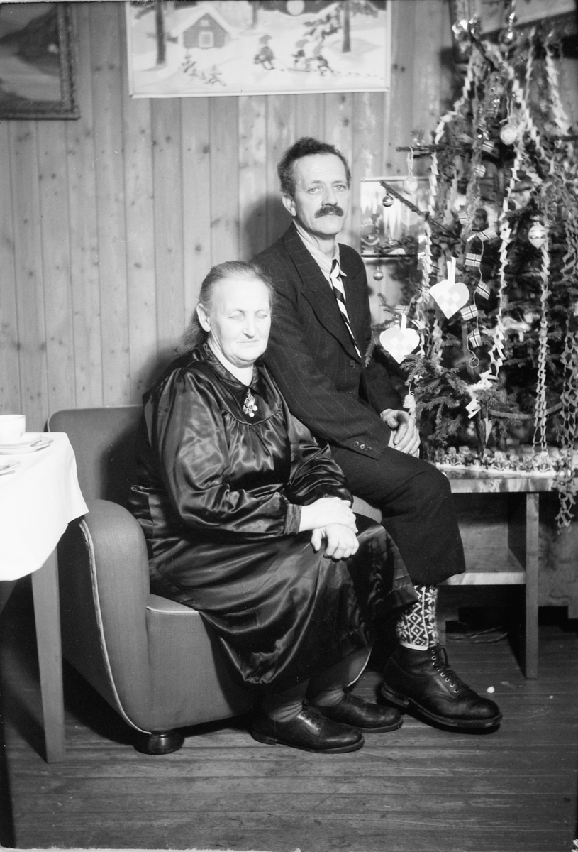 Håkon Prestkværn, Interiør, stue. Sparemøte, Syvertsen. Ukjent kvinne og mann foran juletre.