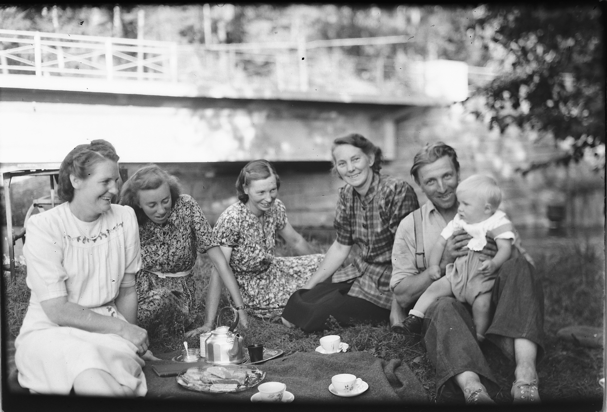 Håkon Prestkværn, Fem kvinner og en mann med et barn på fanget drikker kaffe ute på plenen med kjele og kopper.