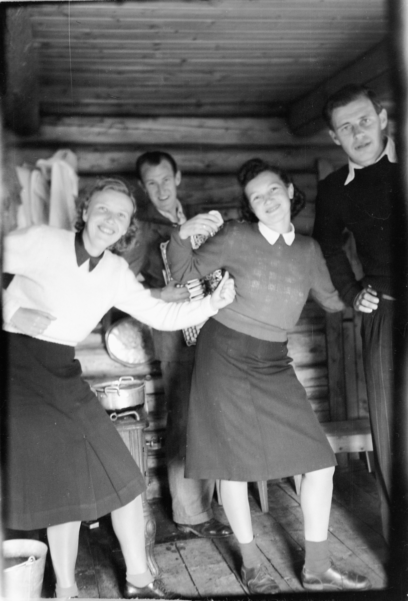 Håkon Prestkværn, Interiør, hytte. To kvinner danser mens en mann spiller trekkspill.