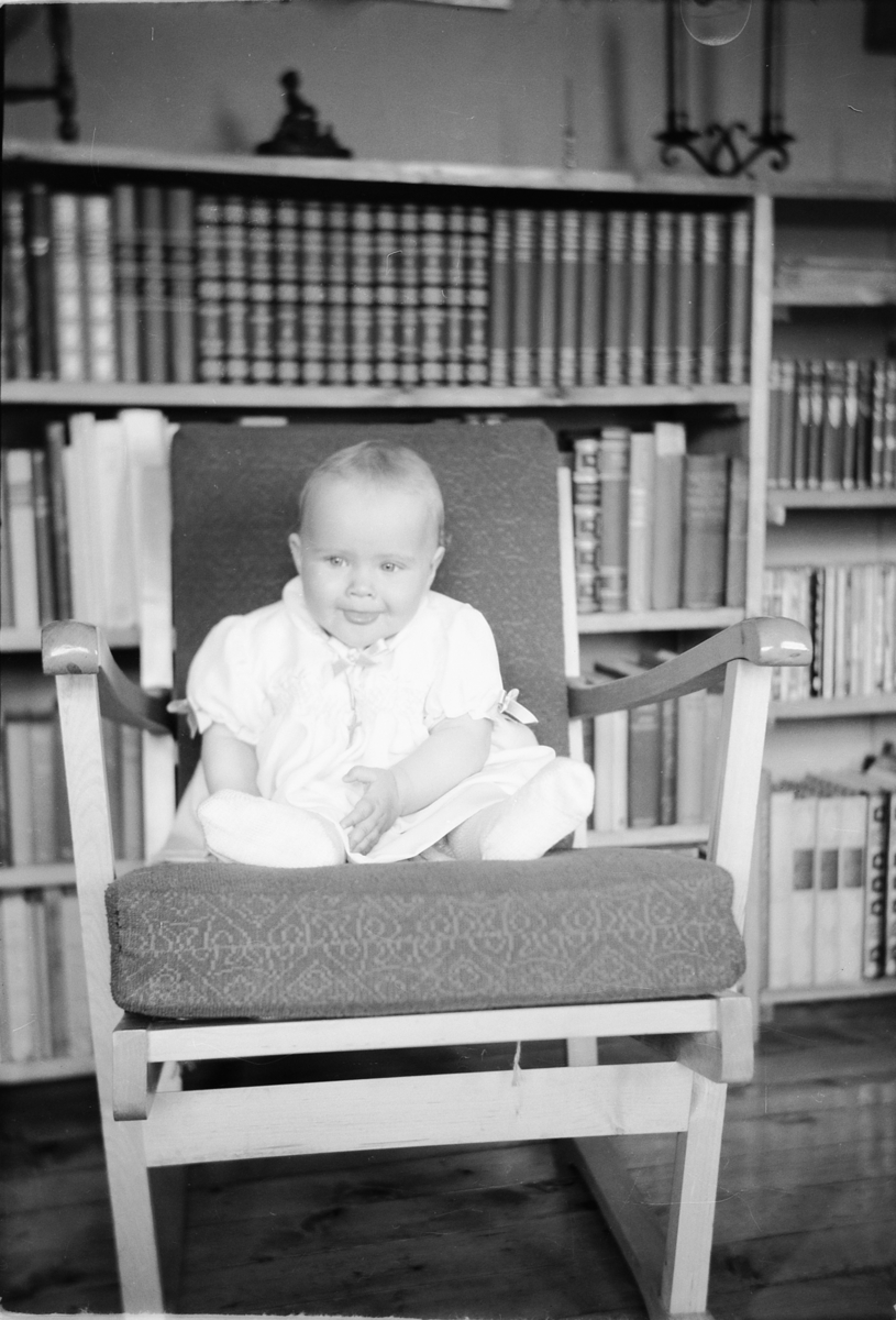 Håkon Prestkværn, En baby sitter i en stol foran en bokhylle.
