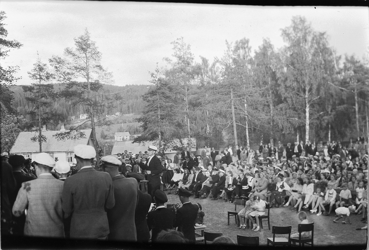 Håkon Prestkværn, Ringsaker sang- og musikklagsstevne, Moelv 1948. Friluftskonserten i Folkets Hus park. Stor forsamling hører på musikkorps spiller på Folkets Hus i Moelv.