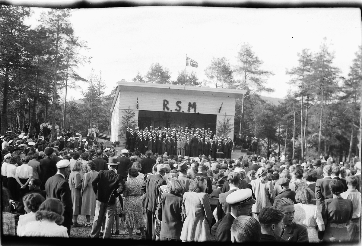 Håkon Prestkværn, Stor gruppe mennesker hører musikkorps spille på Folkets Hus i Moelv. Ringsaker sang- og musikklagsstevne, Moelv 1948. Friluftskonserten i Folkets Hus park.