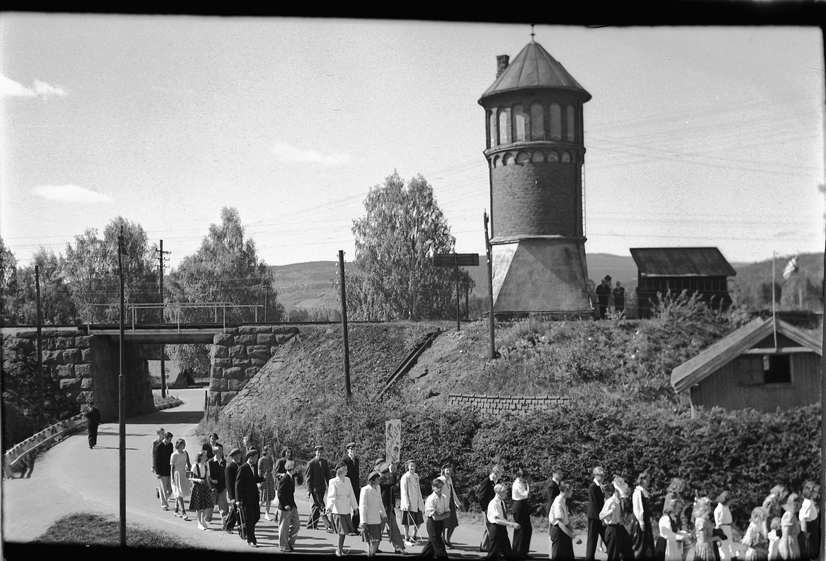 Håkon Prestkværn, 17. mai-tog i Storgata, Moelv. Vanntårnet ved Moelv jernbanestasjon i bakgrunnen.