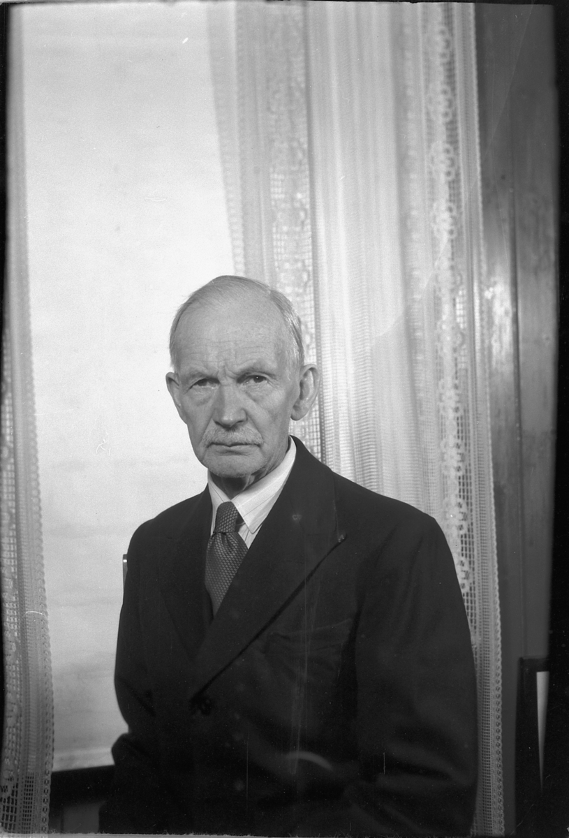 Håkon Prestkværn, Eldre mann foran vindu med gardiner.