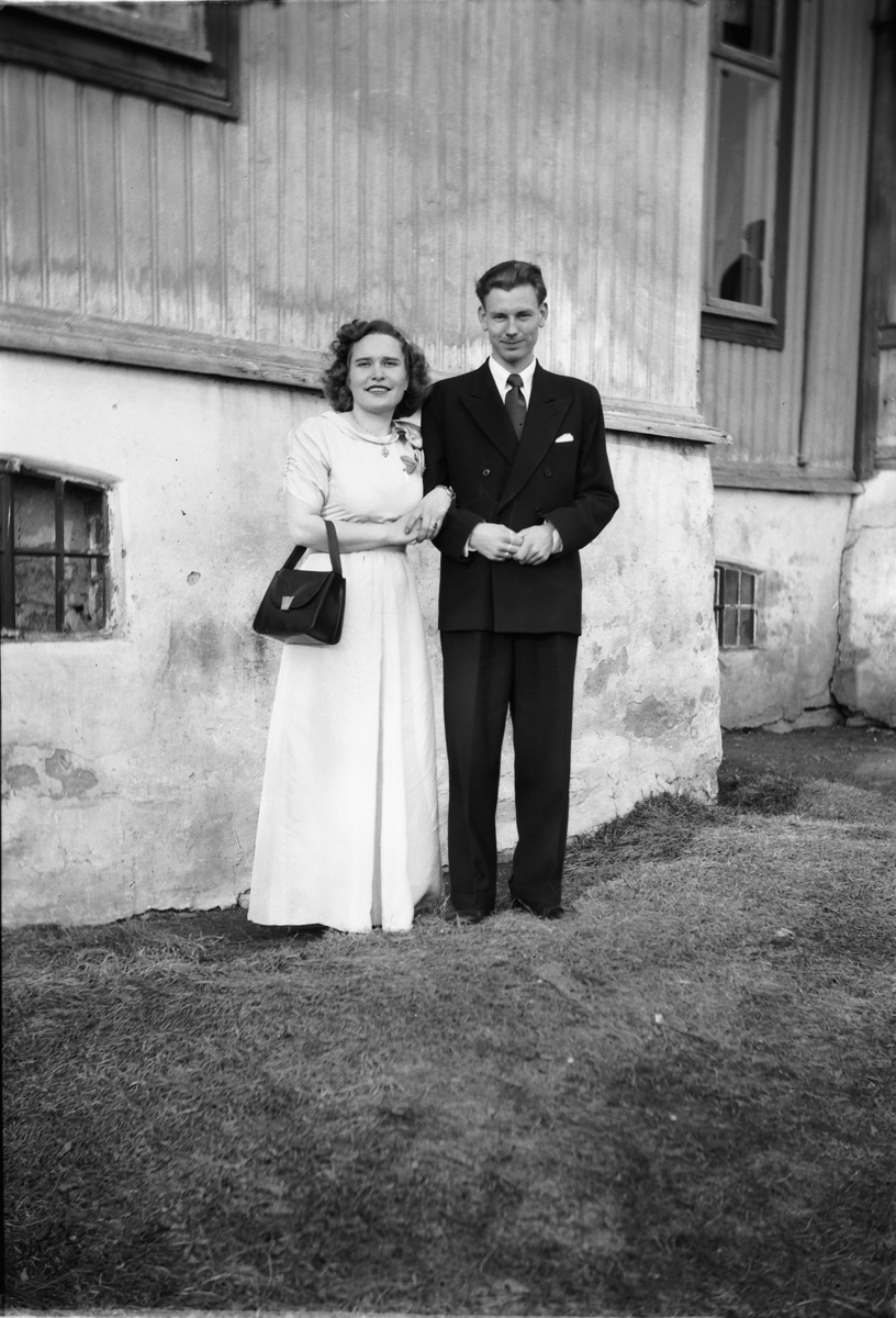 Håkon Prestkværn, Kvinne i kjole og mann i dress ved husveggen.