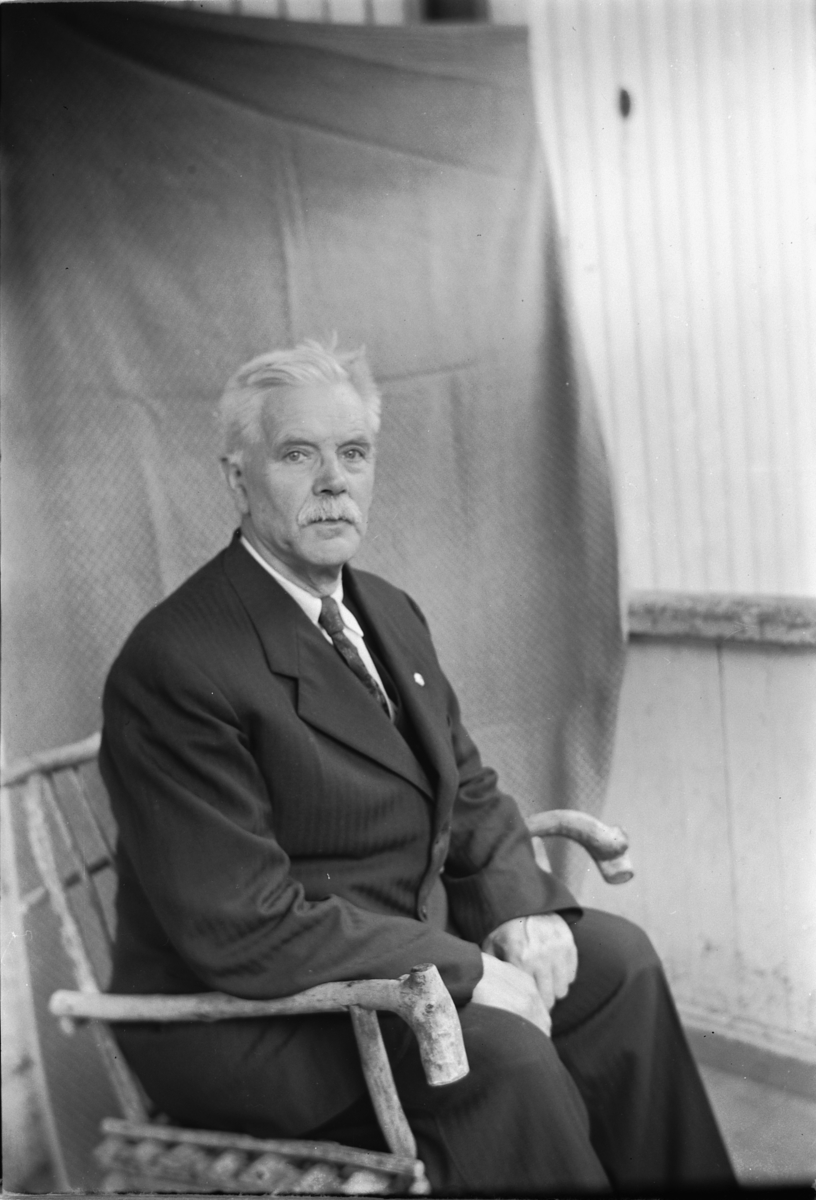 Håkon Prestkværn, Eldre mann i dress sitter på en stol.