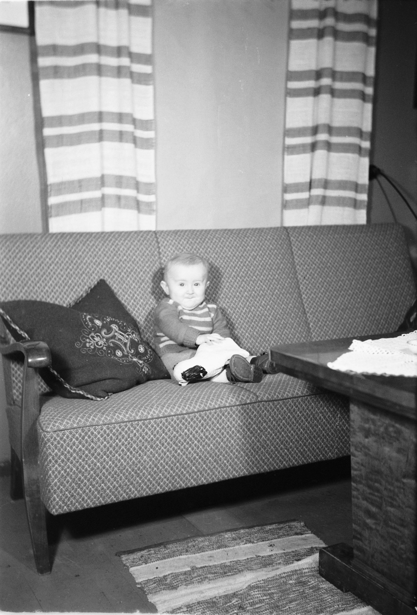 Håkon Prestkværn, Interiør, stue. Baby i en sofa med en leke.