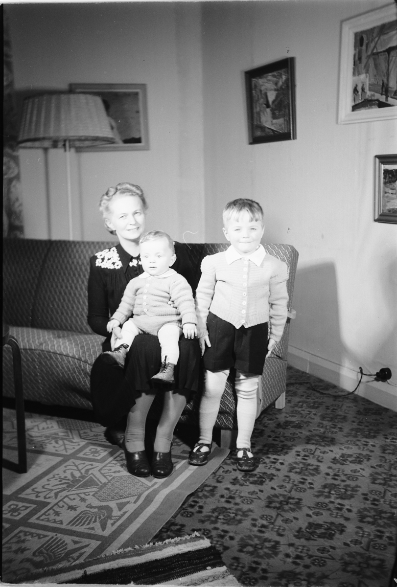 Håkon Prestkværn, Interiør, stue. Eldre kvinne med to barn i en sofa.