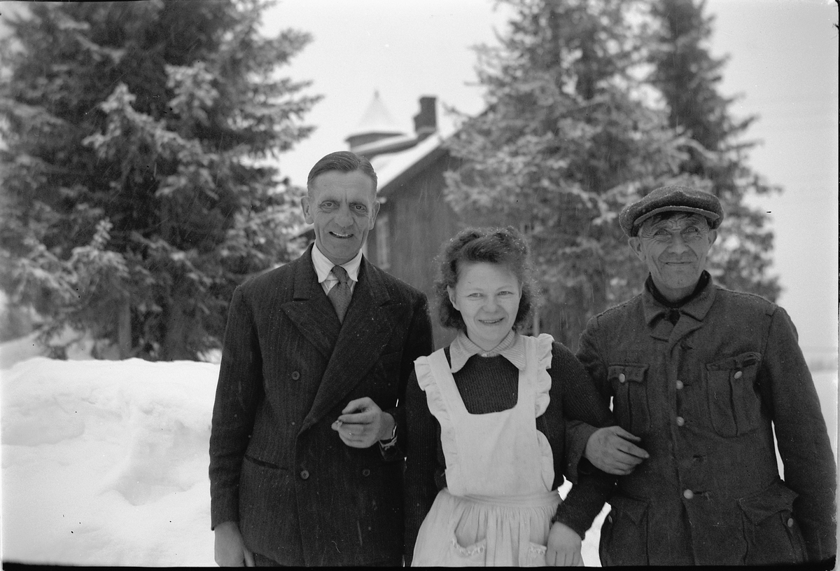 Håkon Prestkværn, To eldre menn med ei kvinne foran et hus.