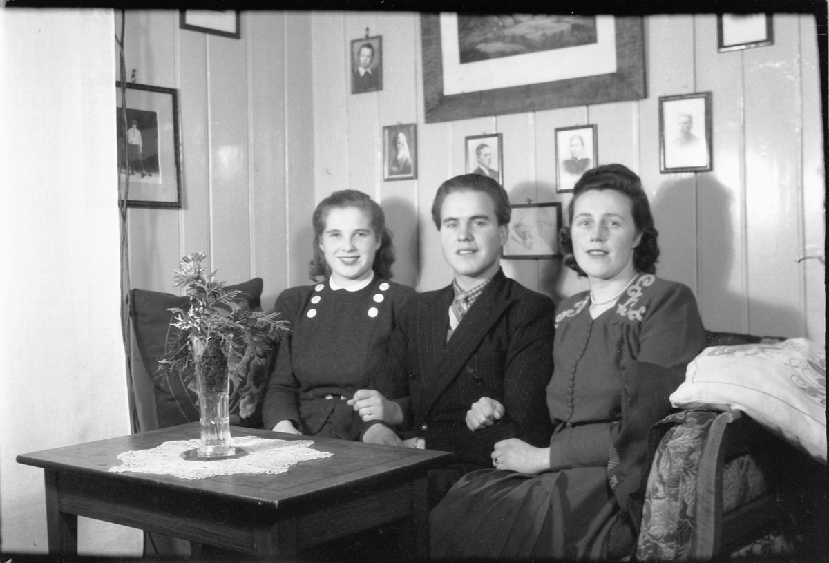 Håkon Prestkværn, Interiør, stue. To kvinner og en mann sitter i sofaen.