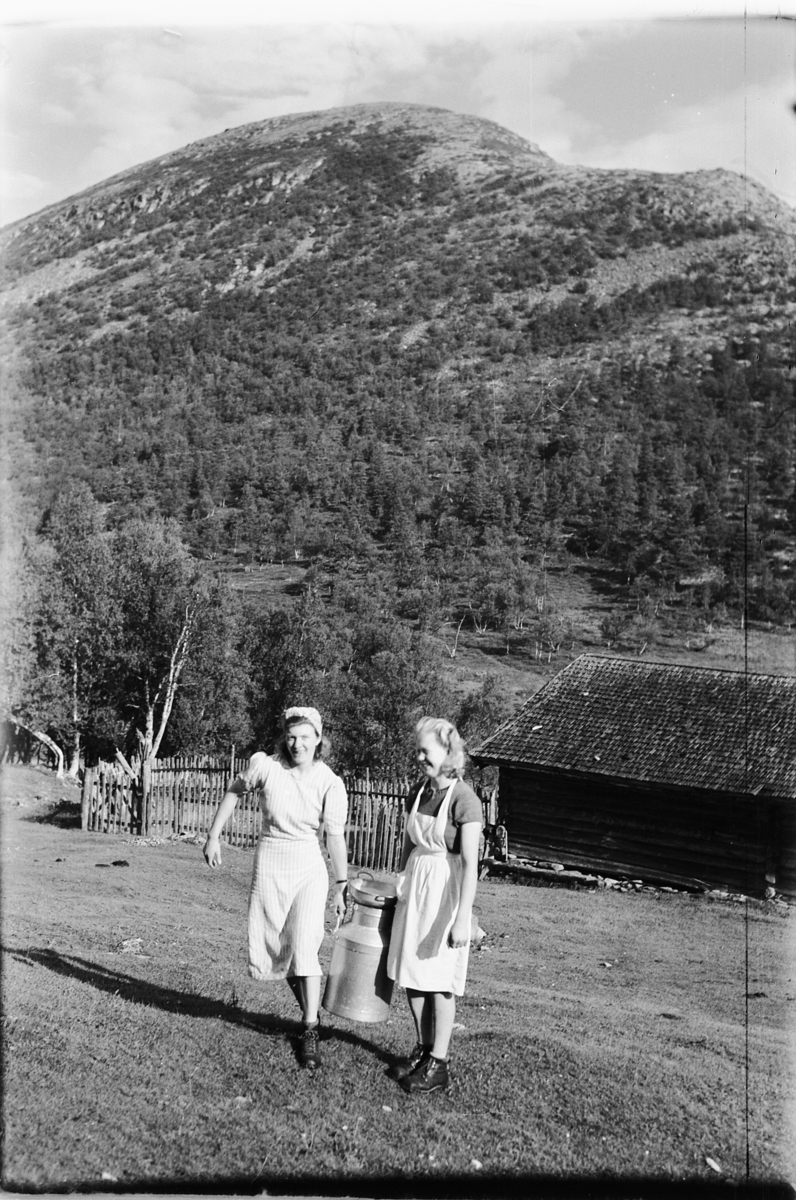 Håkon Prestkværn, To kvinner som bærer et melkespann. melkespann, seter, Rondane, ukjent. Fotokonvolutt mrk. "Rondane"