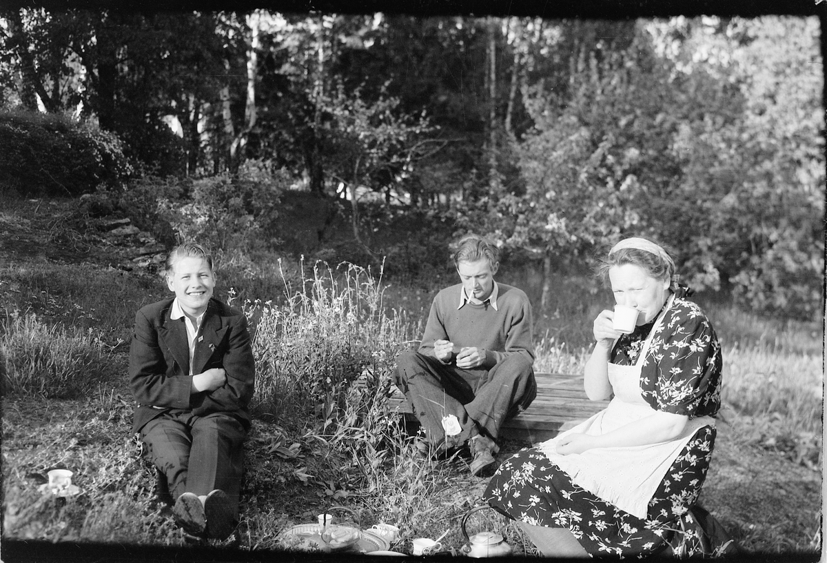 Håkon Prestkværn, To menn og ei kvinne drikker kaffe under en piknik.