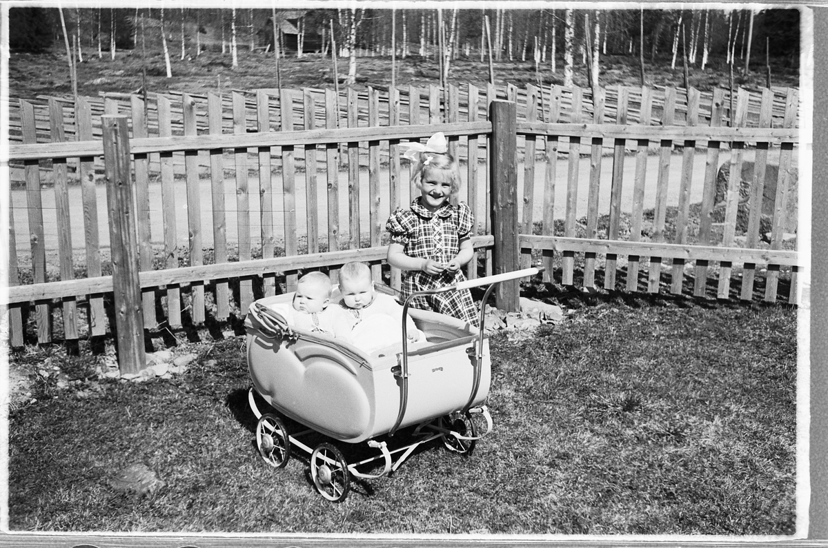 Håkon Prestkværn, Tvillingene i vogna er Knut og Bjørg Svenskerud f. 1949. Jenta med sløyfe er Inger Svenskerud f. 1945. Bildet er tatt ved Åsmarka kirkestue. Jente med sløyfe i håret og to babyer i barnevogn.