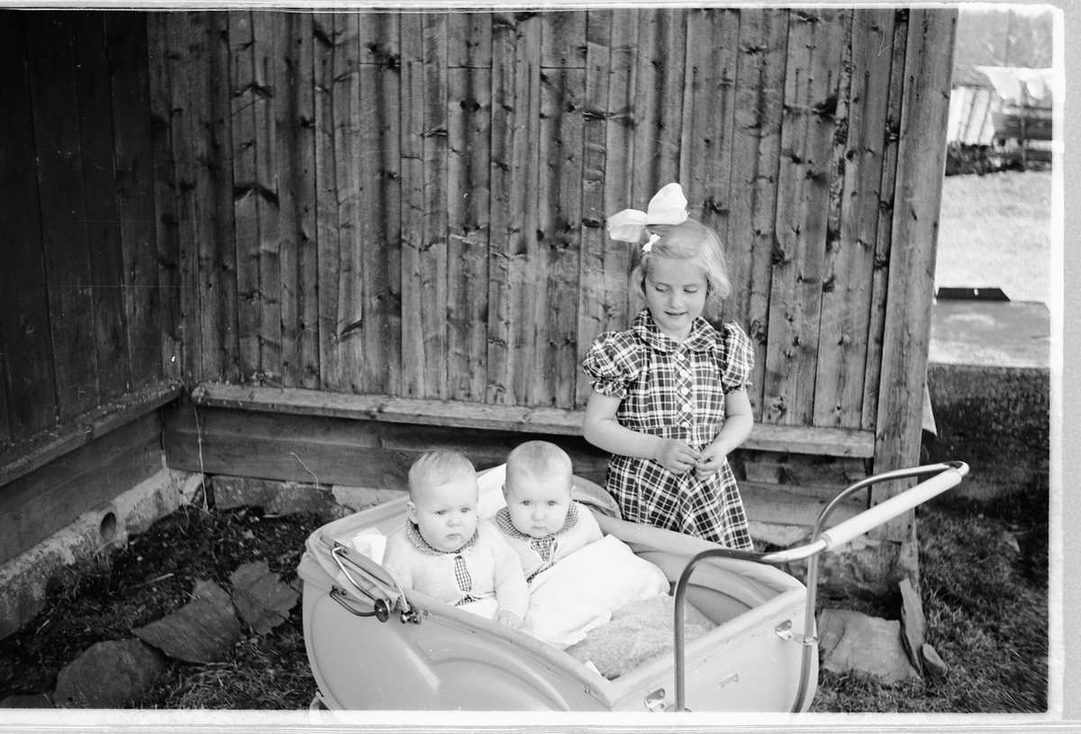 Håkon Prestkværn, Tvillingene i vogna er Knut og Bjørg Svenskerud f. 1949. Jenta med sløyfe er Inger Svenskerud f. 1945. Bildet er tatt ved Åsmarka kirkestue. Jente med sløyfe i håret og to babyer i barnevogn.