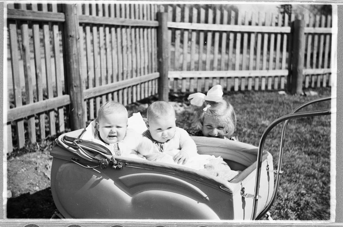 Håkon Prestkværn, To babyer i en bagnevogn og ei jente med sløyfe i håret. Tvillingene i vogna er Knut og Bjørg Svenskerud f. 1949. Jenta med sløyfe er Inger Svenskerud f. 1945. Bildet er tatt ved Åsmarka kirkestue.