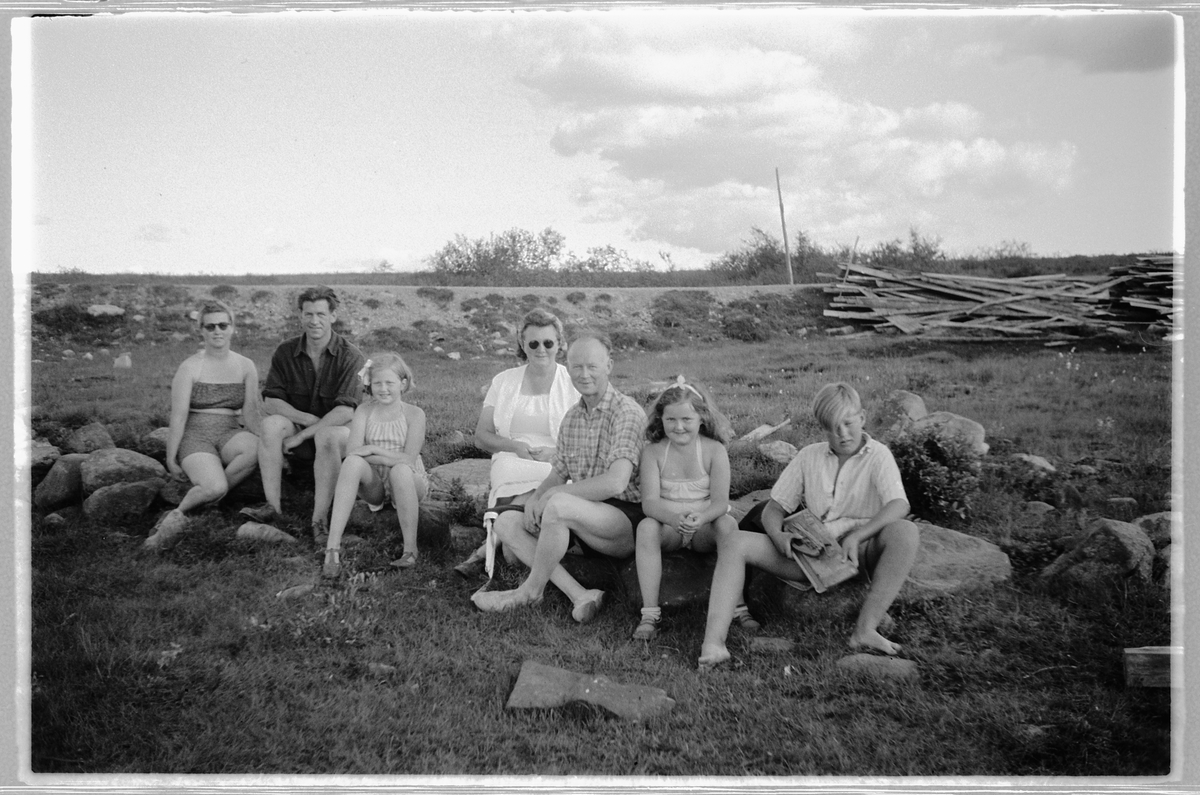 Håkon Prestkværn, Gruppe kvinner, menn og barn sitter på noen steiner.