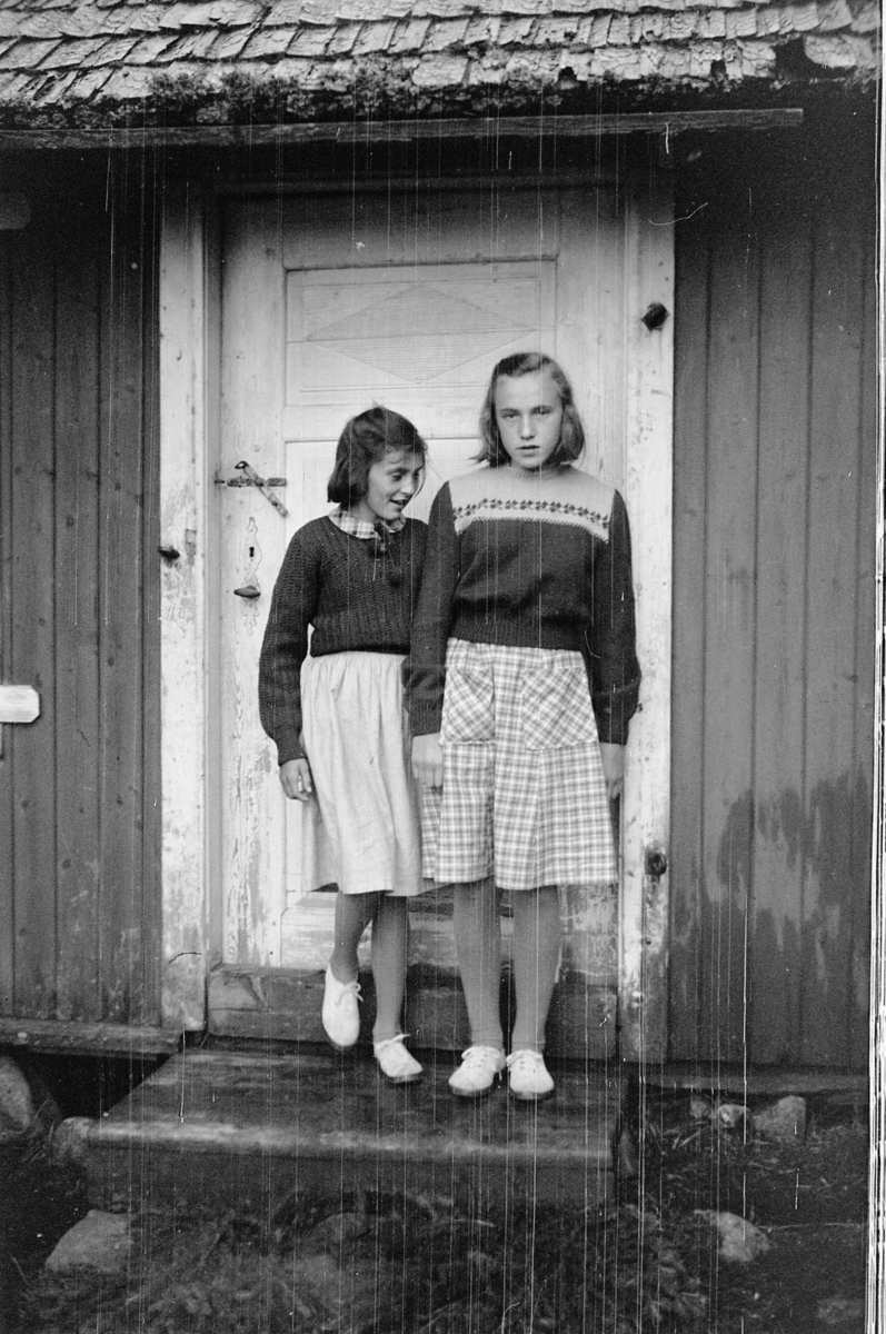 Håkon Prestkværn, To jenter ved inngangsdøra til et hus.