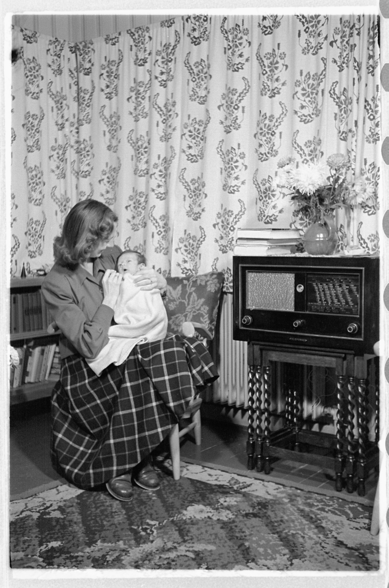 Håkon Prestkværn, Interiør, stue. Kvinne med en baby på fanget. Radio.