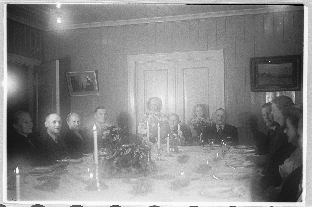 Håkon Prestkværn, Interiør, stue. Kvinner og menn sitter pyntet ved et dekket bord.