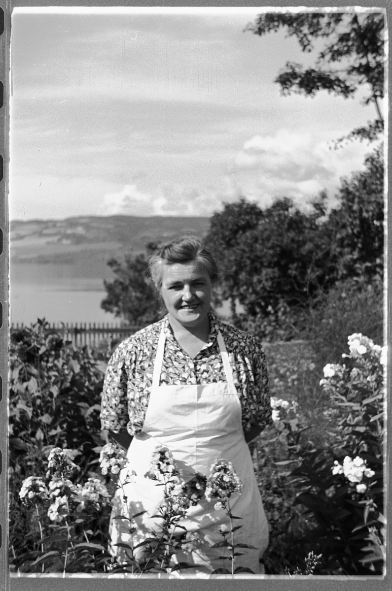 Håkon Prestkværn, Eksteriør, hage. Ukjent kvinn med forkle ved noen blomster.