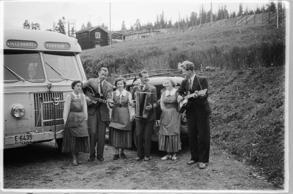 Håkon Prestkværn, Tre menn spiller gitar og trekkspill, mens tre kvinner lytter ved en buss med skilt Lillehammer turvogn. T. h. Ulf Sæhli på gitar. Volvo buss E-6435.