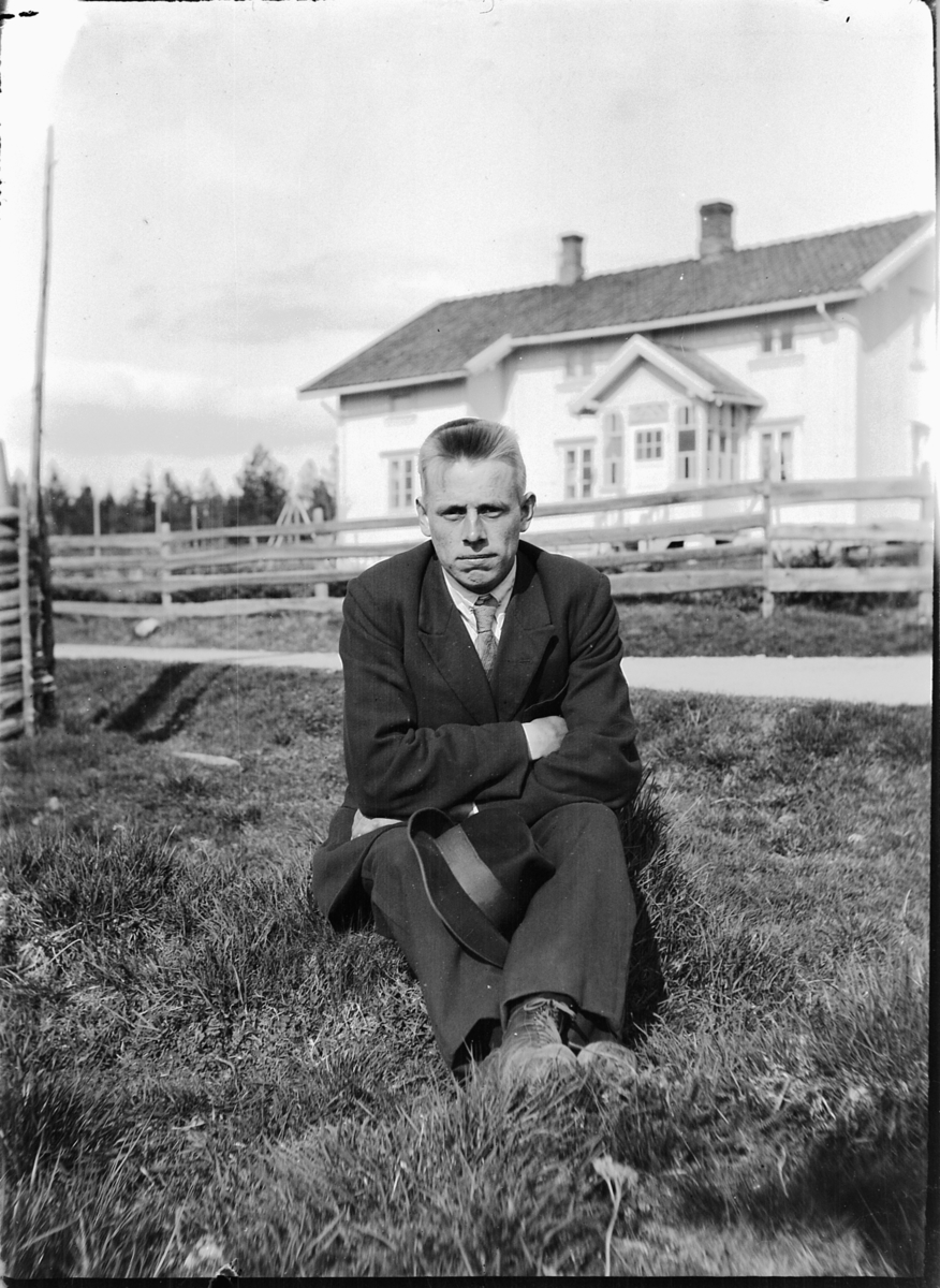 Ole M Martinsen, En mann med dress og hatt, i bakgrunnen et hus med gjerde.