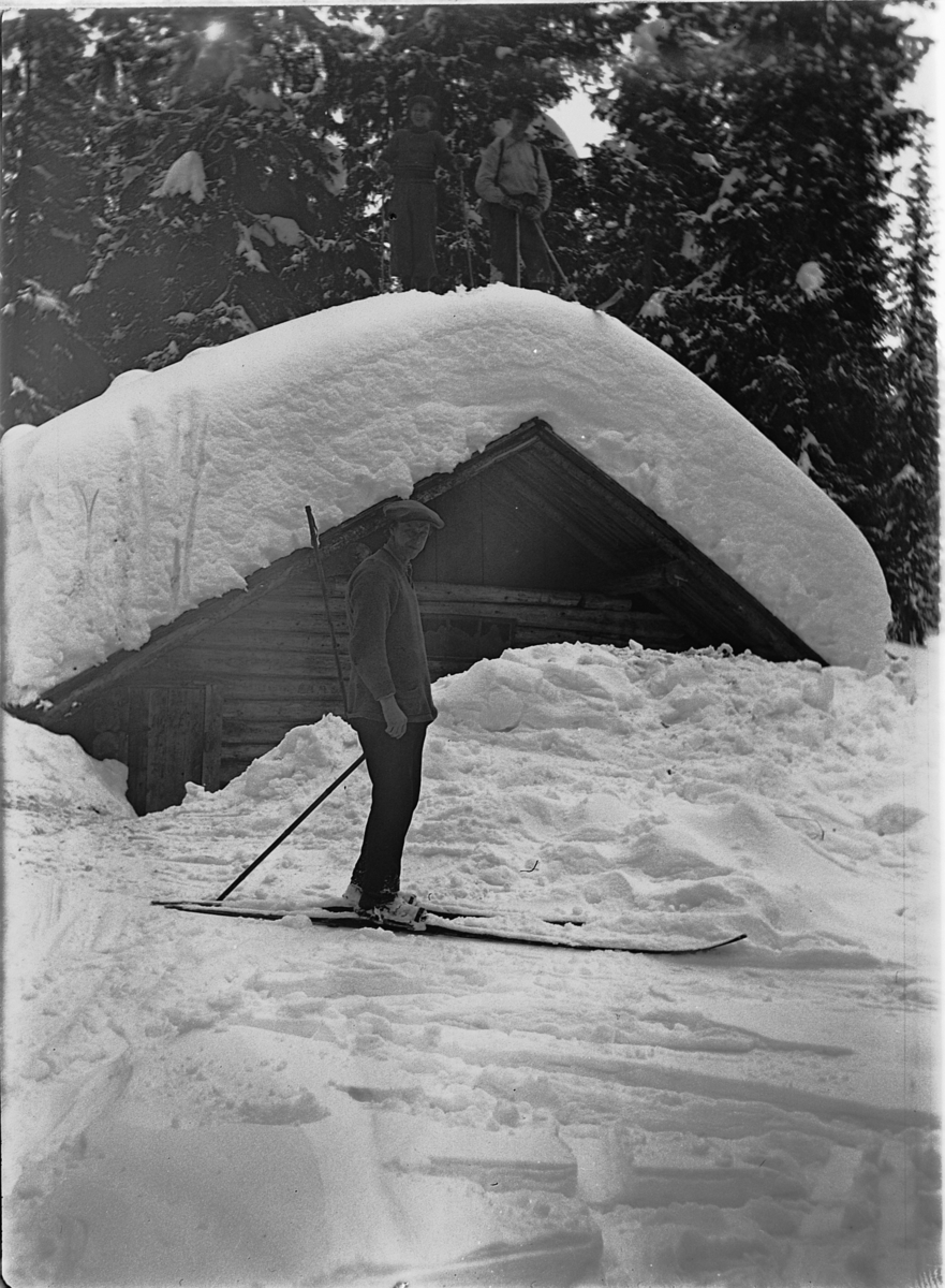 Ole M Martinsen, En mann på ski utenfor ei tømmerkoie i skogen.