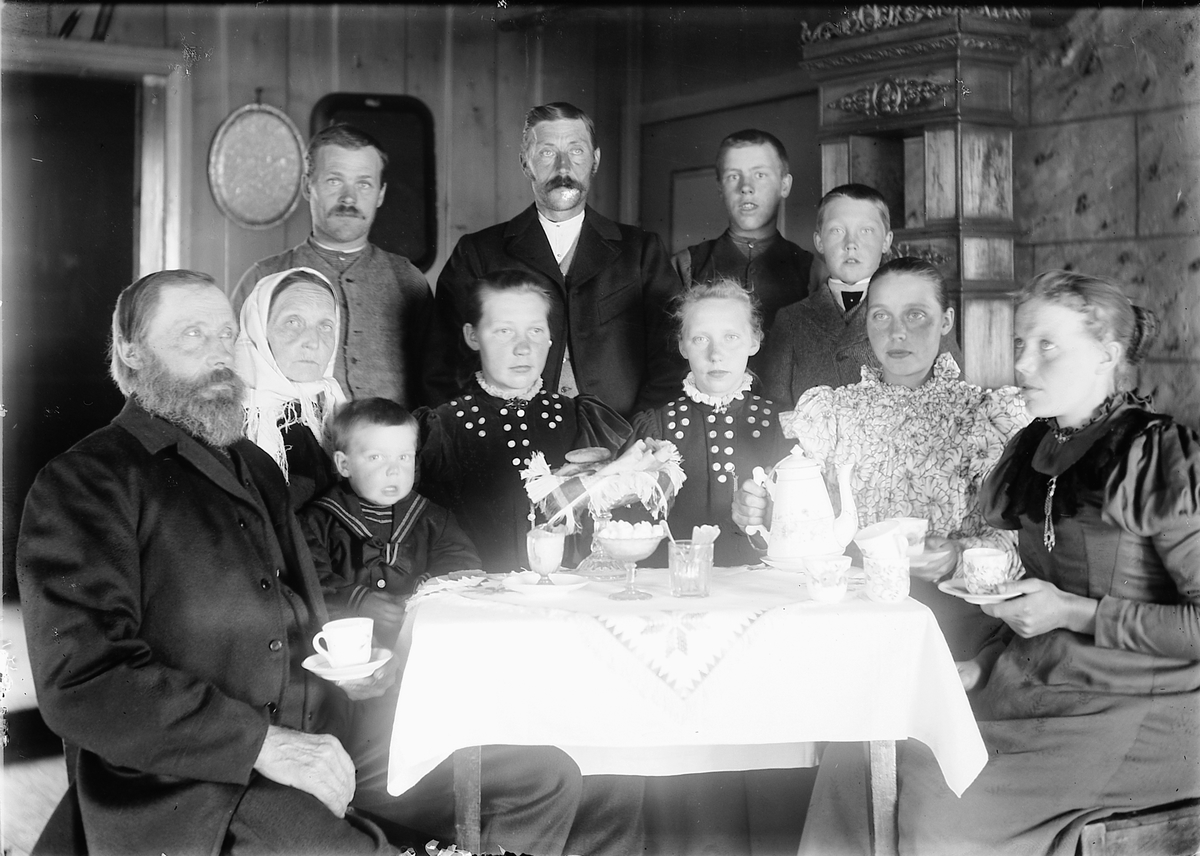 Kristoffer Horne, Interiør, stue. Gruppe menn, kvinner og barn samlet rundt et bord drikker kaffe.