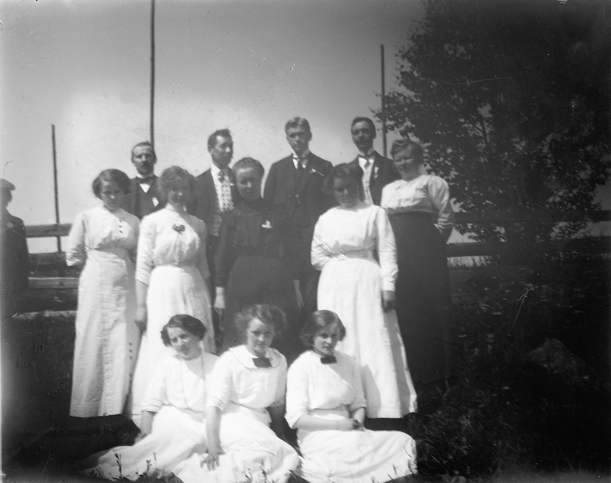 Johs. (Johannes) Johannessen, Gruppe kvinner og menn foran en skigard. Sittende fra venstre: Lovise Johannessen, Aagot Morbech, Anna Marie Johannessen