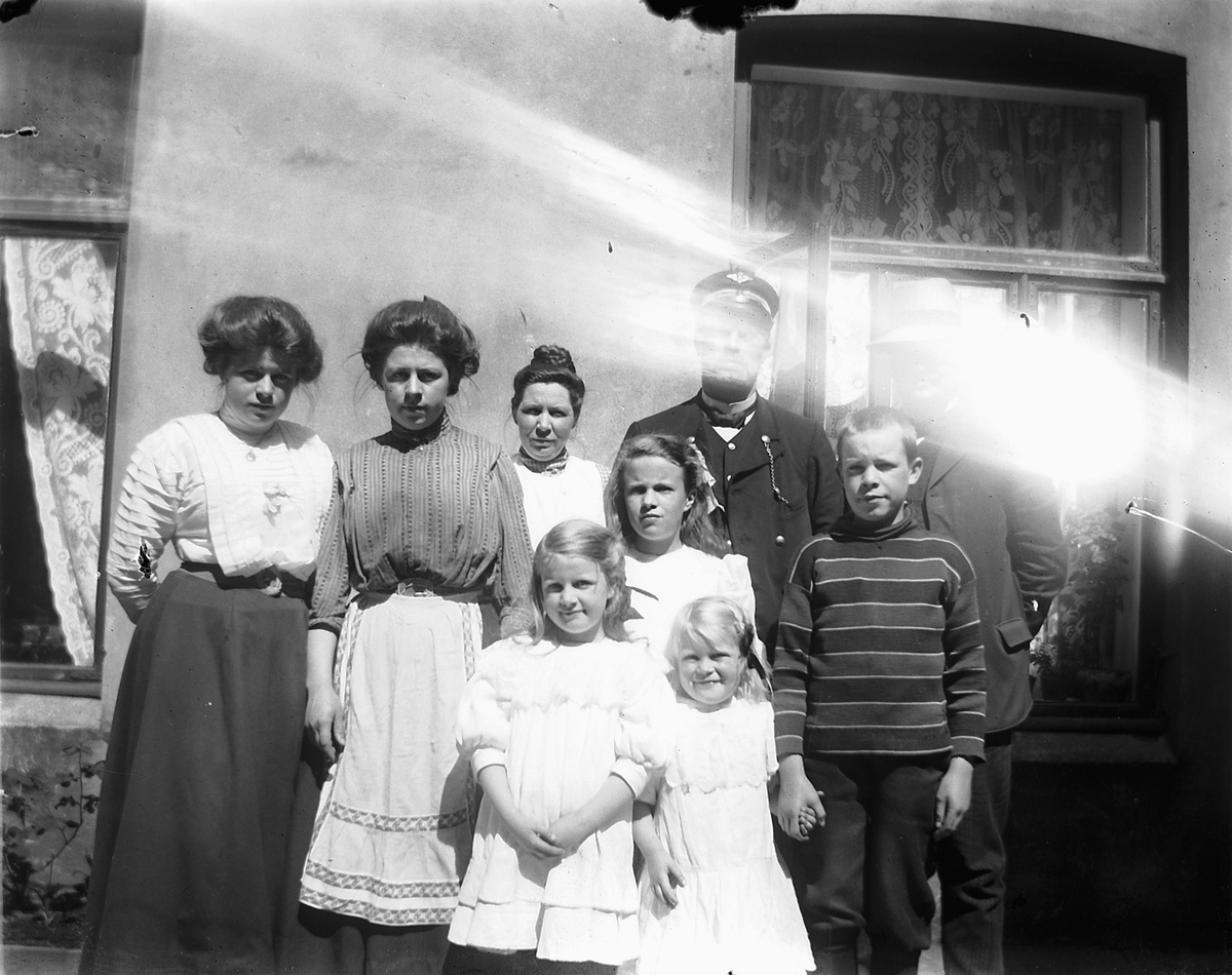 Johs. (Johannes) Johannessen, Kvinner og barn sammen med en togkonduktør ved en husvegg.