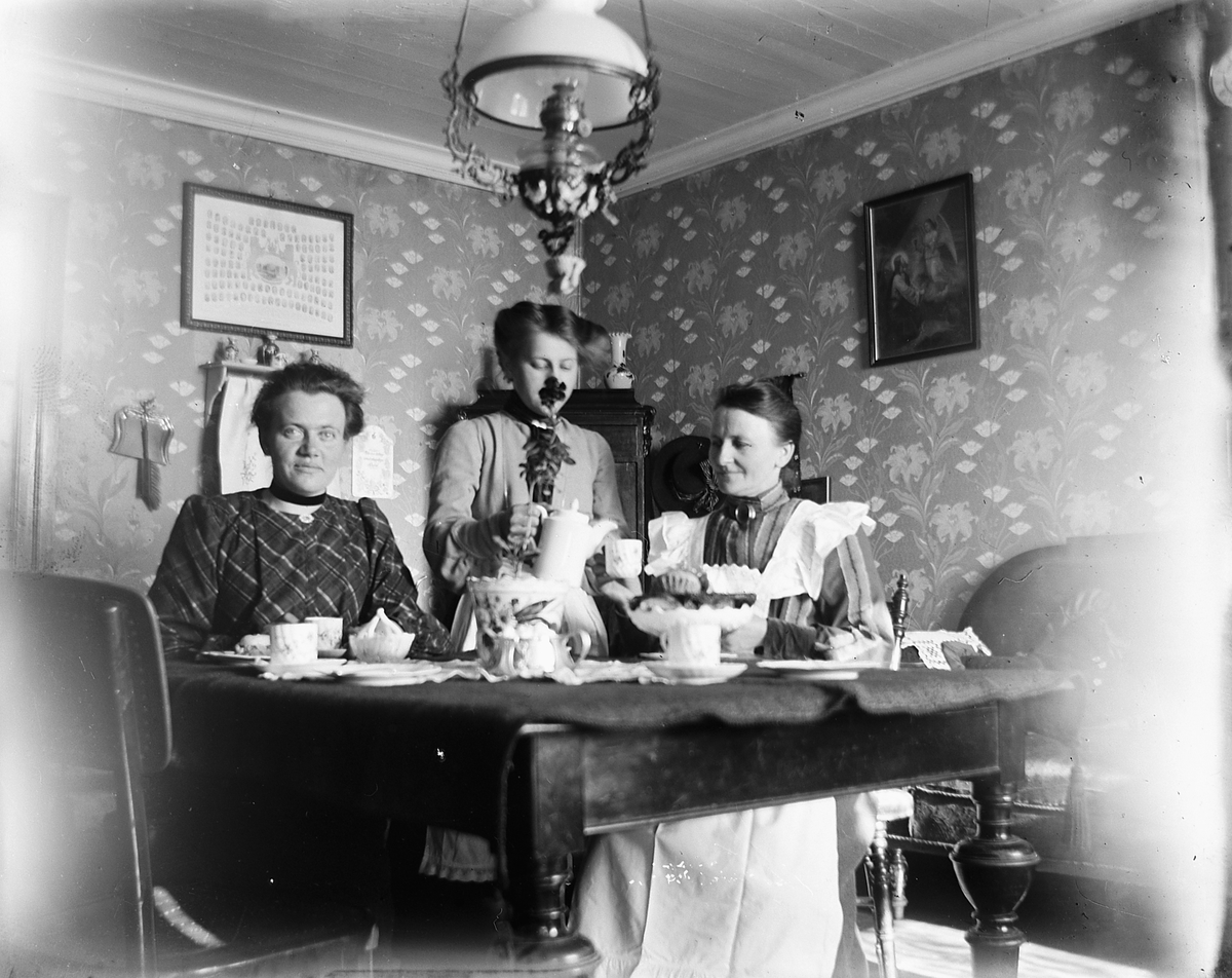 Johs. (Johannes) Johannessen, Interiør, stue. Kaffeservise. Fra høyre: Fru bakermester Lovise Larsdatter Johannessen(gift med Olaus Johannessen), hennes datter Louise Johannessen, Lydia Paulsdtr. Maurud(datter av Paul Larsen Maurud på Helgøya som er Lovise sin bror)