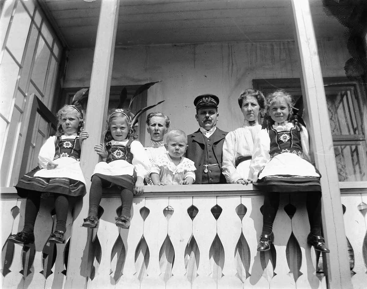Johs. (Johannes) Johannessen, Tre jenter i bunad sammen med to kvinner, et barn, og kaptein Anders Langgaard fra mjøsbåten "Skreia" på verandaen i Skappelsgate 4 i Hamar. Fru Nyquist?
