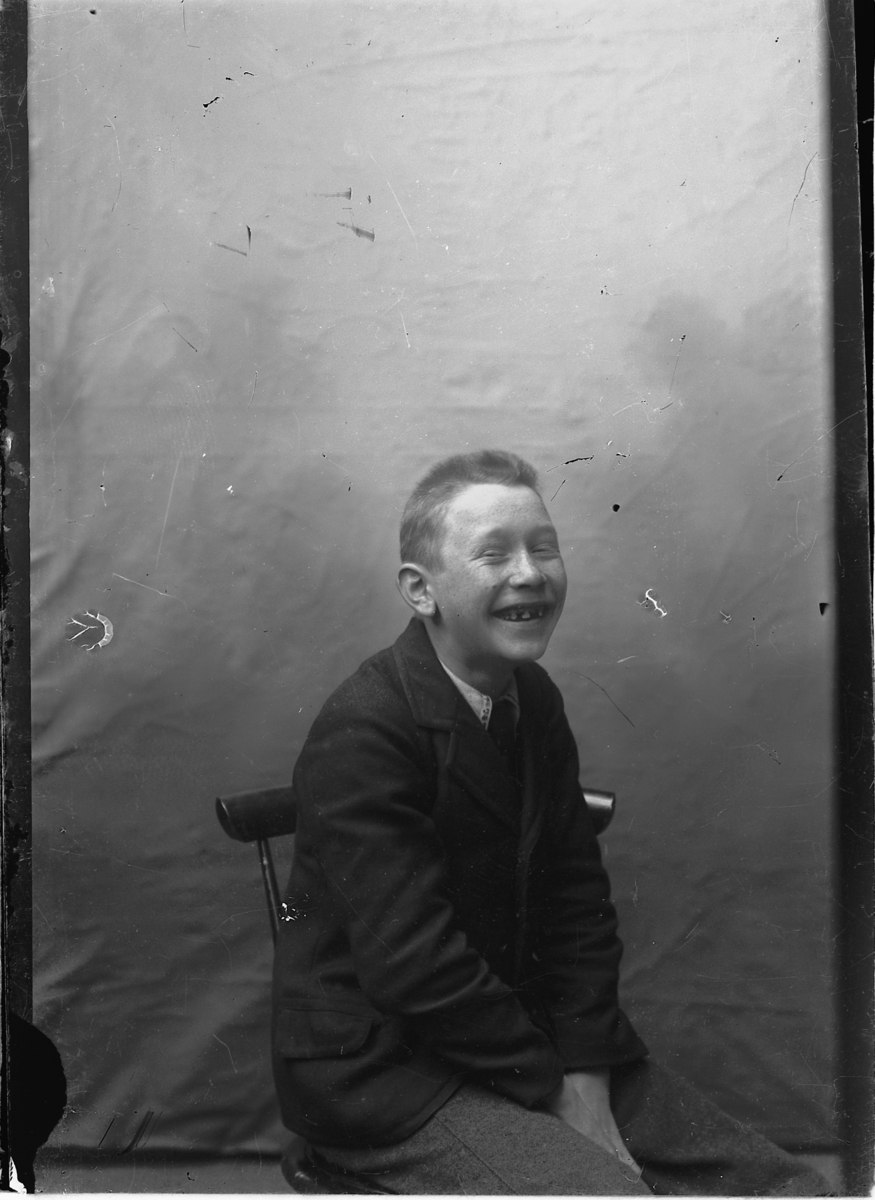 Ragnvald Andersen, Portrett, leende gutt på stol i studio. Ukjent.