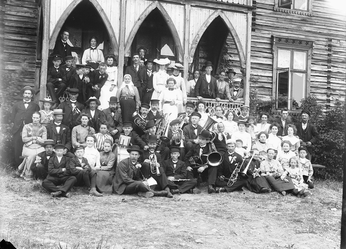Ragnvald Andersen, Kjelsrud gård, Helgøya. Jernbanemusikken med familie på tur. Stor gruppe foran inngangspartiet. Instrumenter.