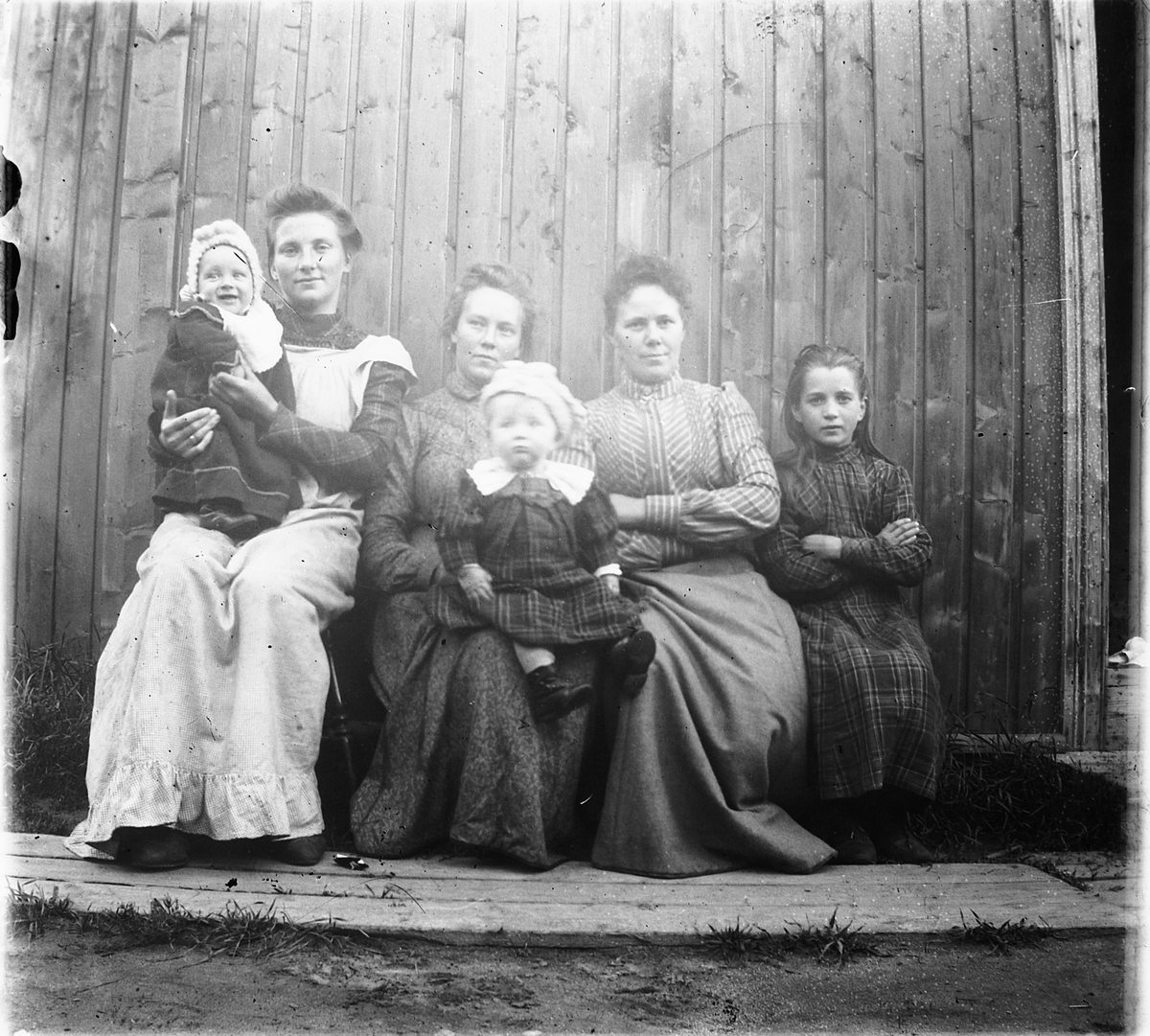 Ragnvald Andersen, Tre kvinner og tre barn sitter i husveggen.