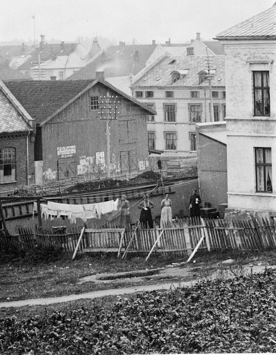 Hans Emil Erichsen, Holset før Håkonsgate gikk til St. Olavsgate. Vangsvegen går foran de to bygningene til venstre, som er Hamar Elektrisitetsverk og H. C. Indahls frølager. Bygget i midten er det som senere ble Hotell Bondeheimen. Fire kvinner ved klær til tørk, klesvask.