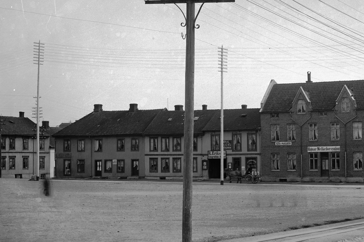 Hans Emil Erichsen, Østre Torg i Hamar med bebyggelsen langs Vangsvegen. Hamar Melkeforsyning, Agra Margarin, R. Eriksens Fotografiske Atelier. J. Skaraasen Agentur. Folk på torget. Hest og kjerre.