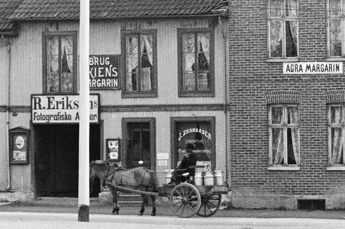 Hans Emil Erichsen, Østre Torg i Hamar med bebyggelsen langs Vangsvegen. Agra Margarin, R. Eriksens Fotografiske Atelier. J. Skaraasen Agentur. Folk på torget. Hest og kjerre.